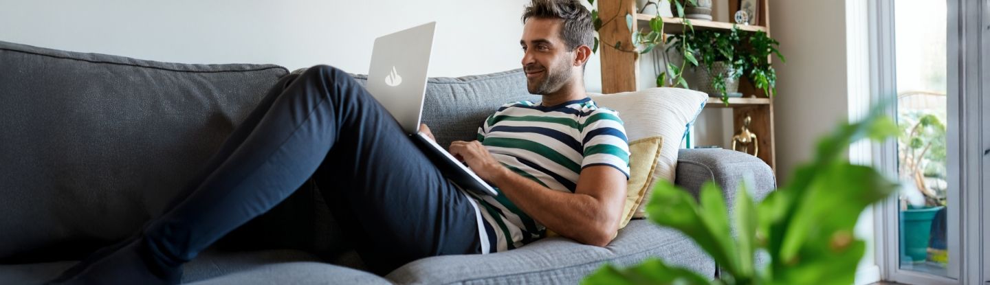 Mann liegt mit Laptop auf dem Sofa.